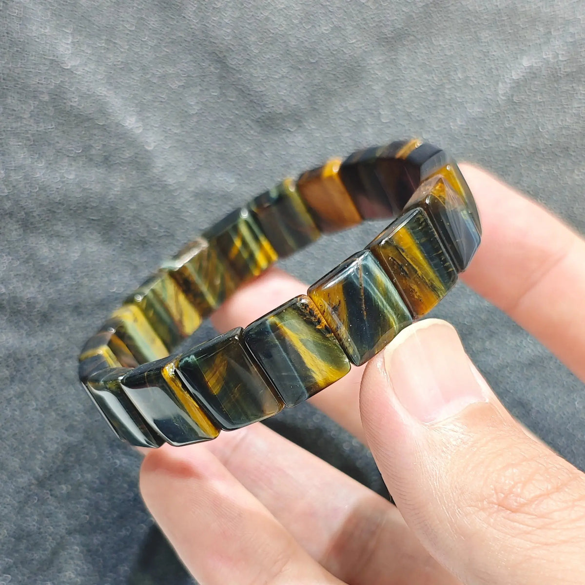 Hand holding a natural blue yellow tiger eye plate bead bracelet displaying golden and indigo chatoyant bands