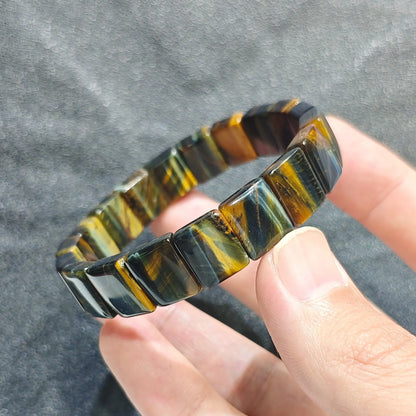 Hand holding a natural blue yellow tiger eye plate bead bracelet displaying golden and indigo chatoyant bands