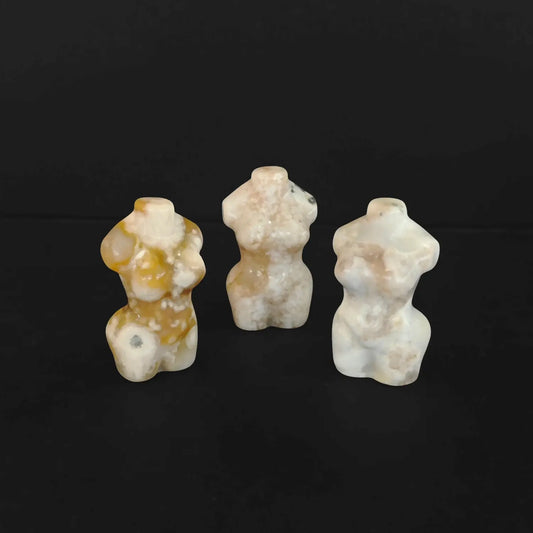 Three natural flower agate goddess torso figurines standing together on a black background displaying unique pink and white floral patterns