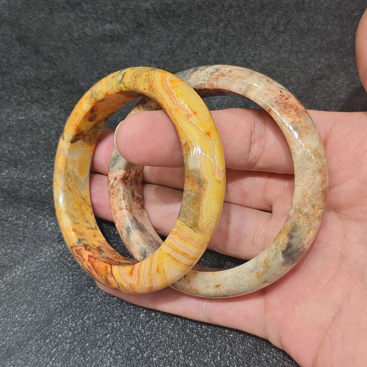 Natural Crazy Lace Agate solid gemstone bangle bracelet held on hand displaying complex yellow and brown flow banding