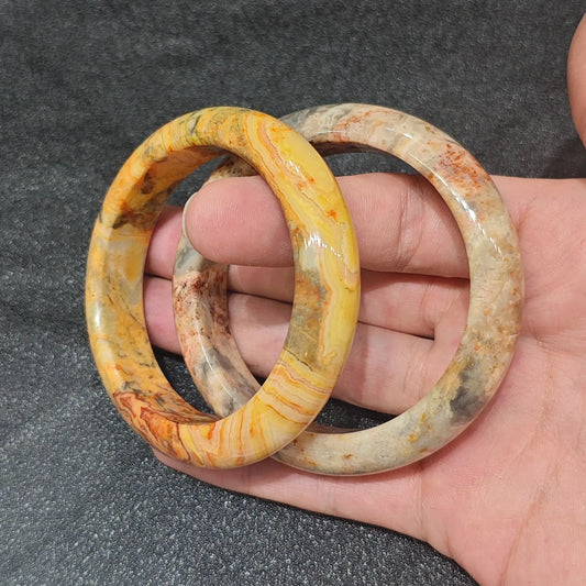 Natural Crazy Lace Agate solid gemstone bangle bracelet held on hand displaying complex yellow and brown flow banding