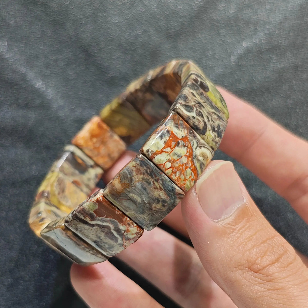 Hand holding a natural crazy lace agate plate bead bracelet displaying earth tone mosaic patterns and chalcedony bands