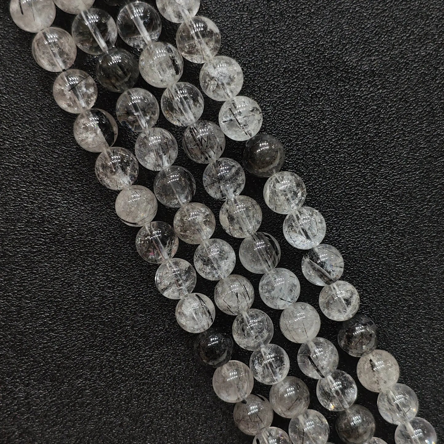 Close up view of natural crystal beads showcasing B grade black rutilated quartz strands with needle tourmaline inclusions on a dark surface