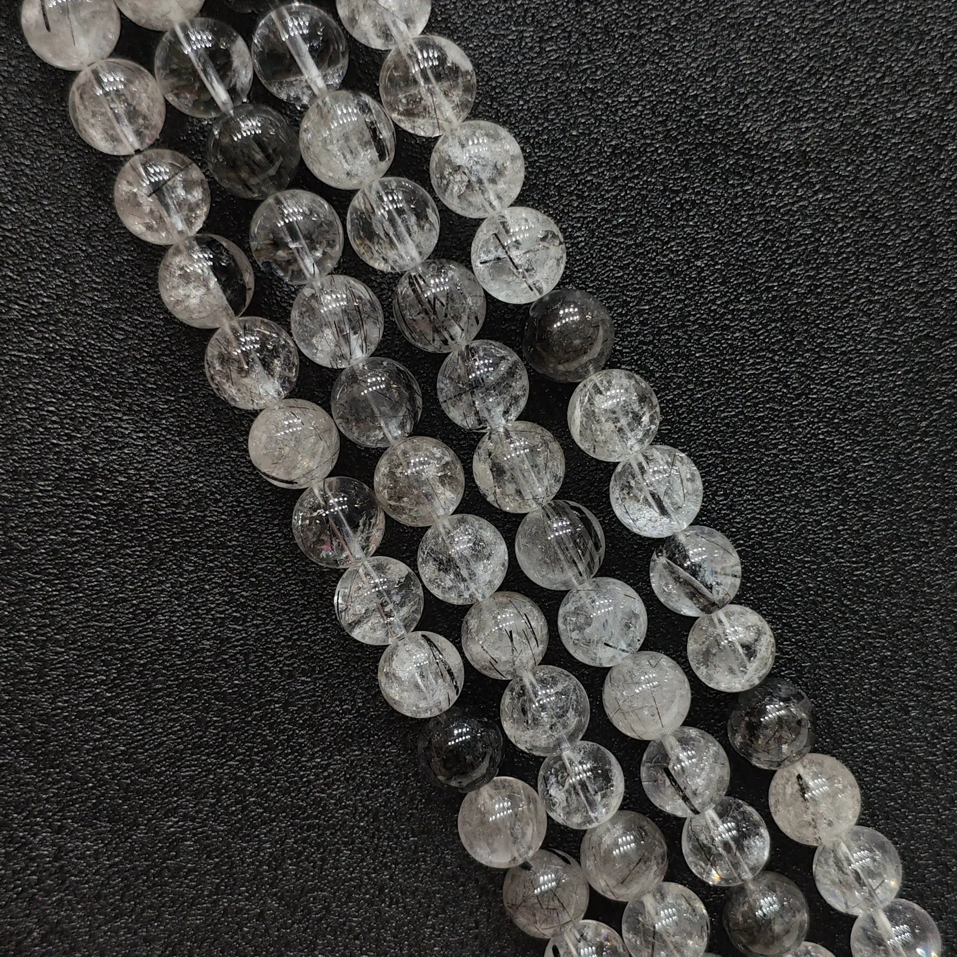 Close up view of natural crystal beads showcasing B grade black rutilated quartz strands with needle tourmaline inclusions on a dark surface