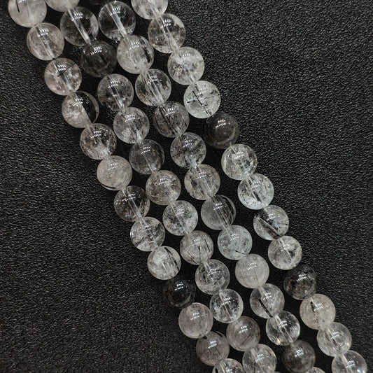 Close up view of natural crystal beads showcasing B grade black rutilated quartz strands with needle tourmaline inclusions on a dark surface