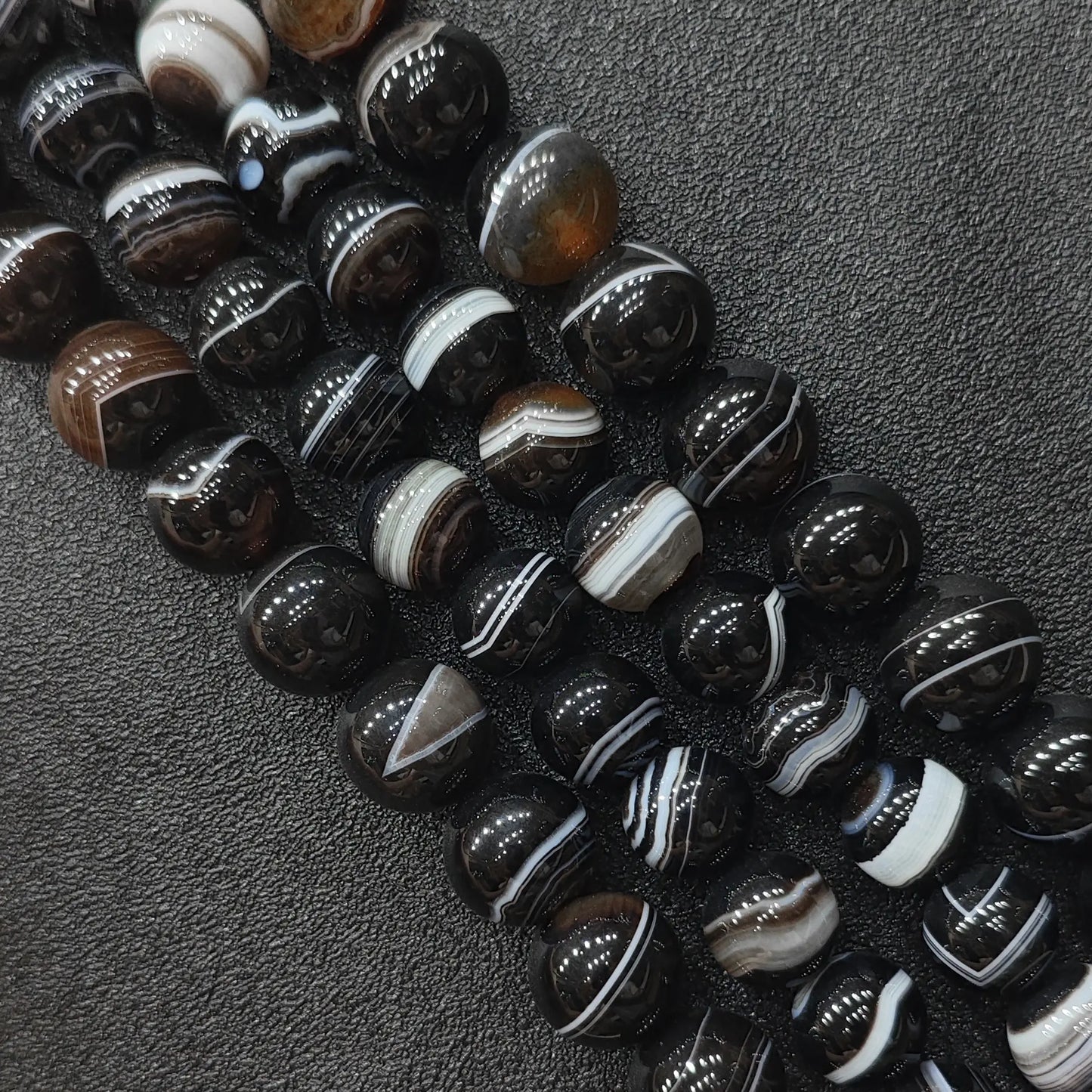 Natural dark brown banded agate round loose beads strands showing crisp striped orbital patterns on a dark background for jewelry making