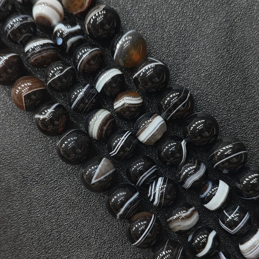 Natural dark brown banded agate round loose beads strands showing crisp striped orbital patterns on a dark background for jewelry making