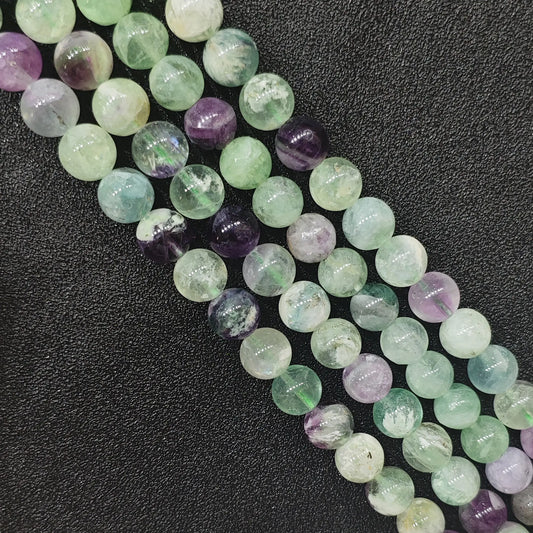 Natural feather fluorite round loose beads strands with soft purple and green hues showing feather-like internal wisps on a dark background