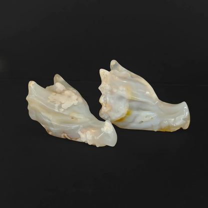 Two natural cherry blossom agate dragon skull crystal carvings displaying intricate white flower plumes on a solid black background