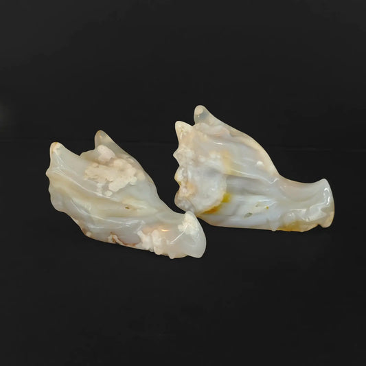 Two natural cherry blossom agate dragon skull crystal carvings displaying intricate white flower plumes on a solid black background