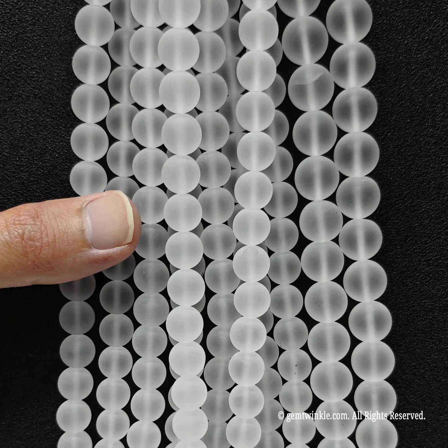 Hand holding multiple strands of natural frosted clear quartz crystal beads to showcase size choice grid