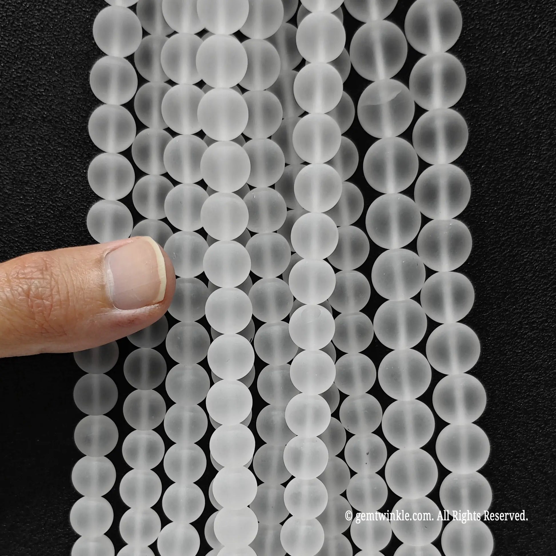 Hand holding multiple strands of natural frosted clear quartz crystal beads to showcase size choice grid