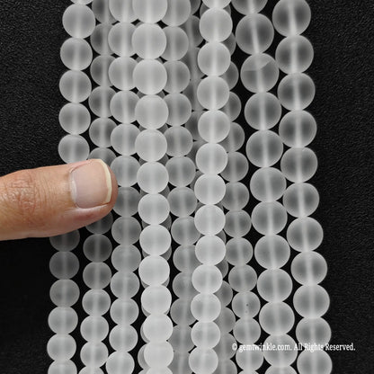 Hand holding multiple strands of natural frosted clear quartz crystal beads to showcase size choice grid