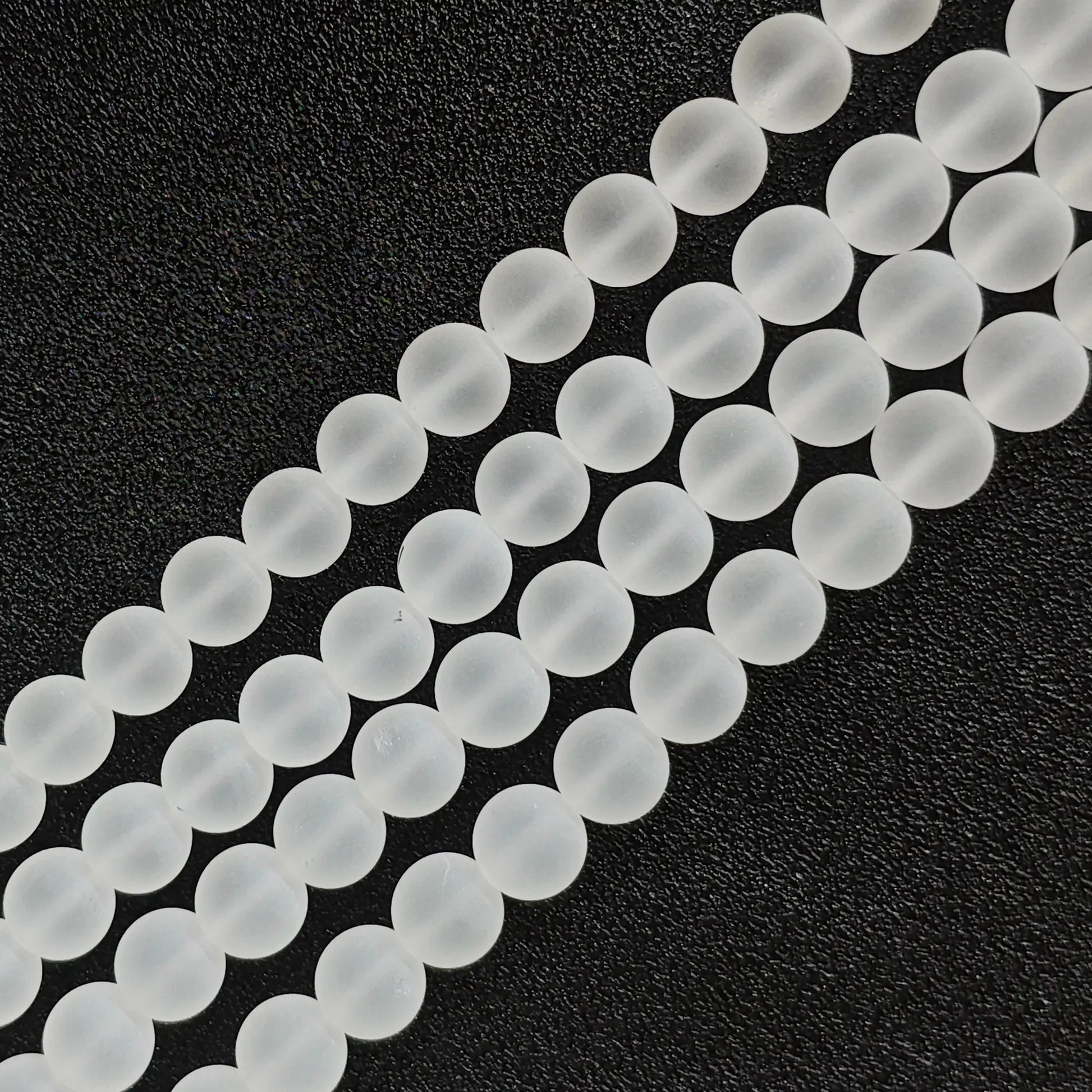 Natural frosted clear quartz matte crystal beads strands arranged diagonally on black background
