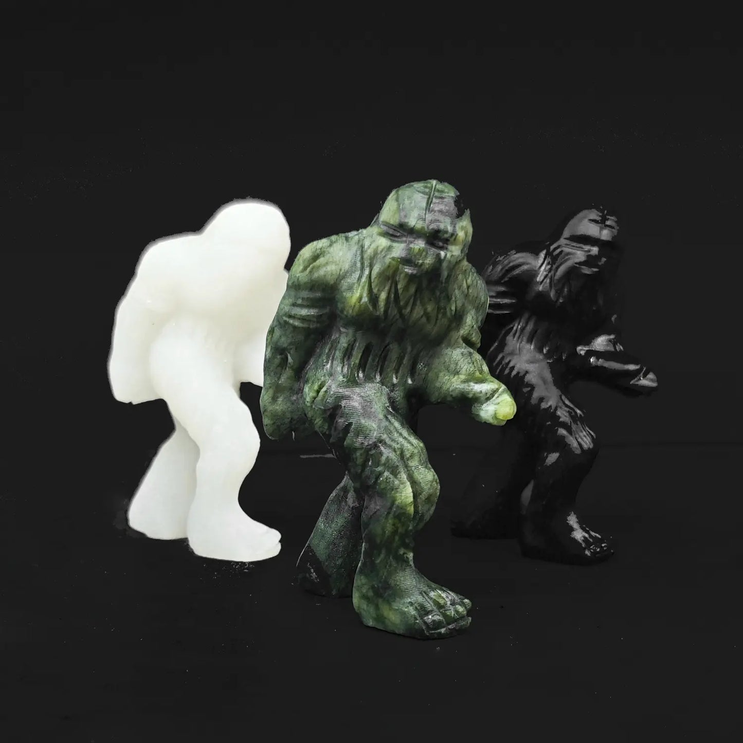 Front view of three natural gemstone bigfoot statues showcasing white marble serpentine stone and black obsidian material variations