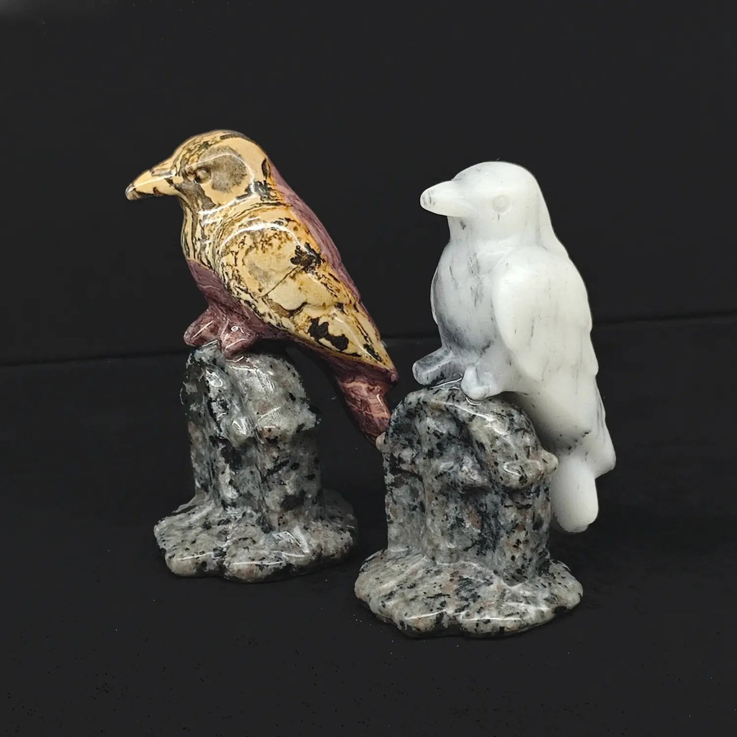 Two 3 inch hand carved natural gemstone gothic raven statues perched on cross tombstone bases made of speckled granite rock on a dark background