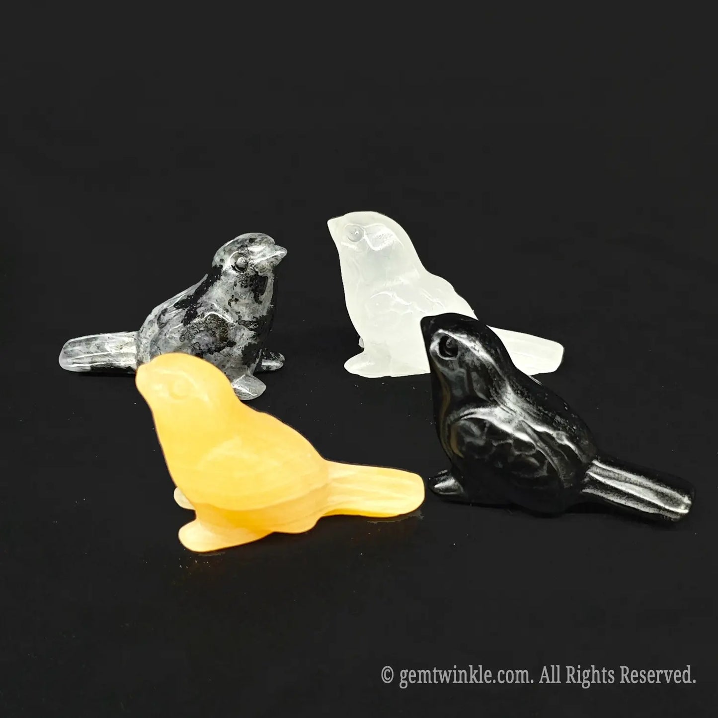 Front view of four natural gemstone tiny bird statues showing heavily included clear quartz yellow calcite black obsidian and spotted grey stone material variations