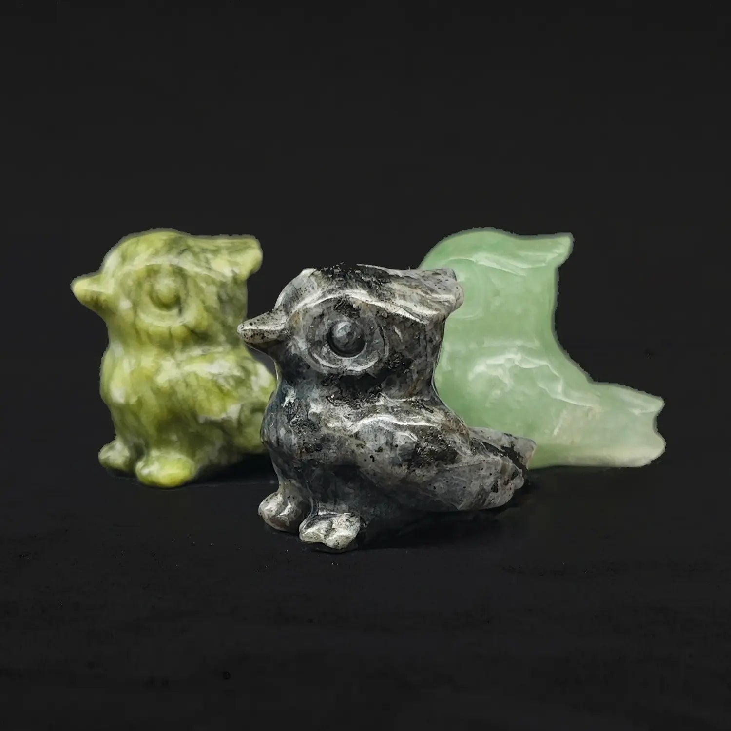 Front view of three natural gemstone tiny owl statues showing green serpentine stone spotted grey stone and green aventurine material variations