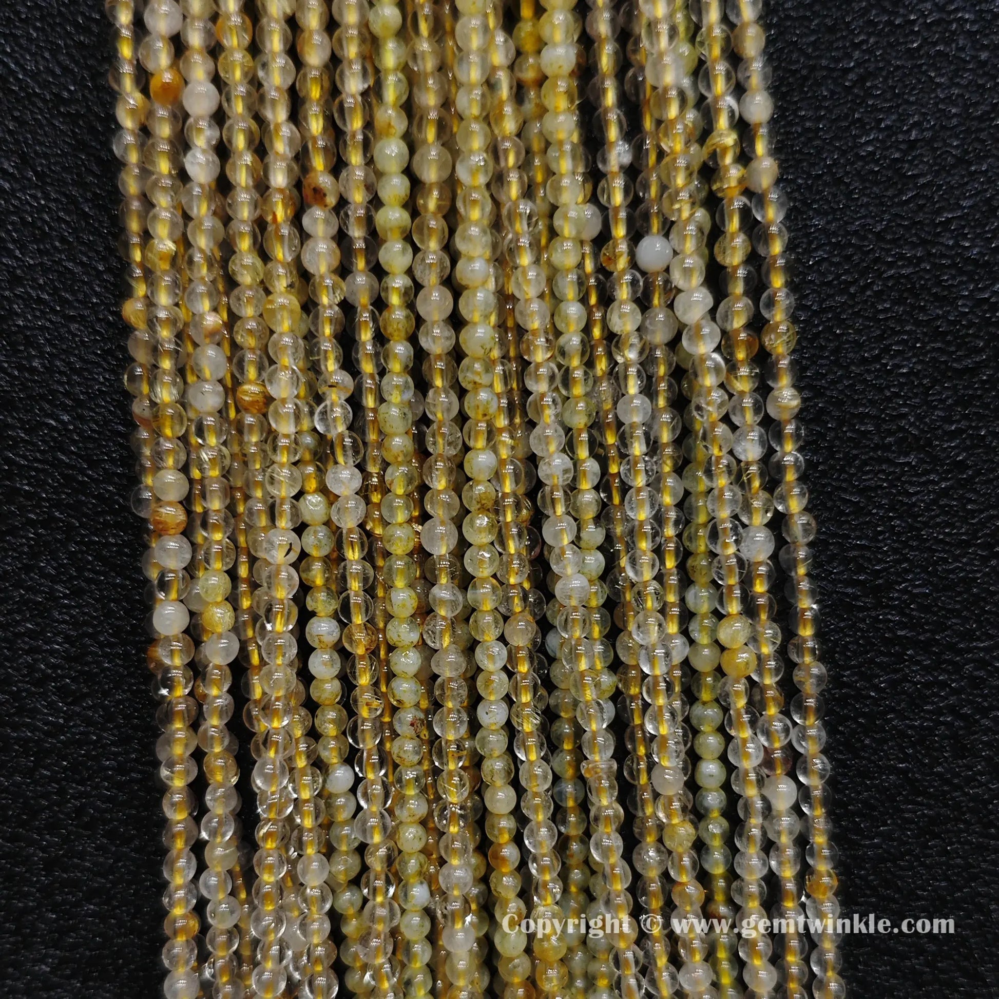Detailed shot of real 2mm small gemstone beads showing heavy internal cracks and scattered golden rutile hair needles on standard cords