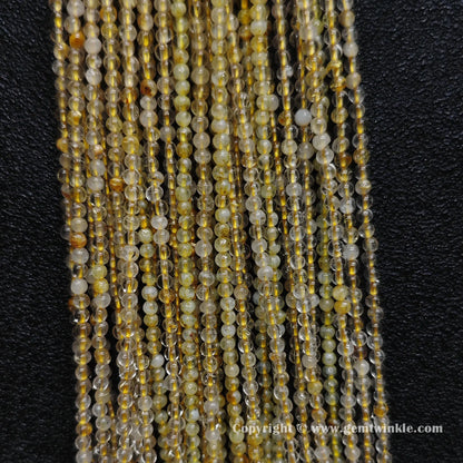 Detailed shot of real 2mm small gemstone beads showing heavy internal cracks and scattered golden rutile hair needles on standard cords