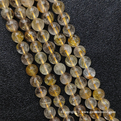 Detailed perspective of commercial grade 8mm gold hair quartz beads with natural internal crystal mist strung on jewelry wire
