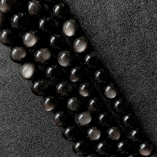 Macro closeup of Grade A natural silver sheen obsidian round beads showing metallic chatoyancy on dark surface