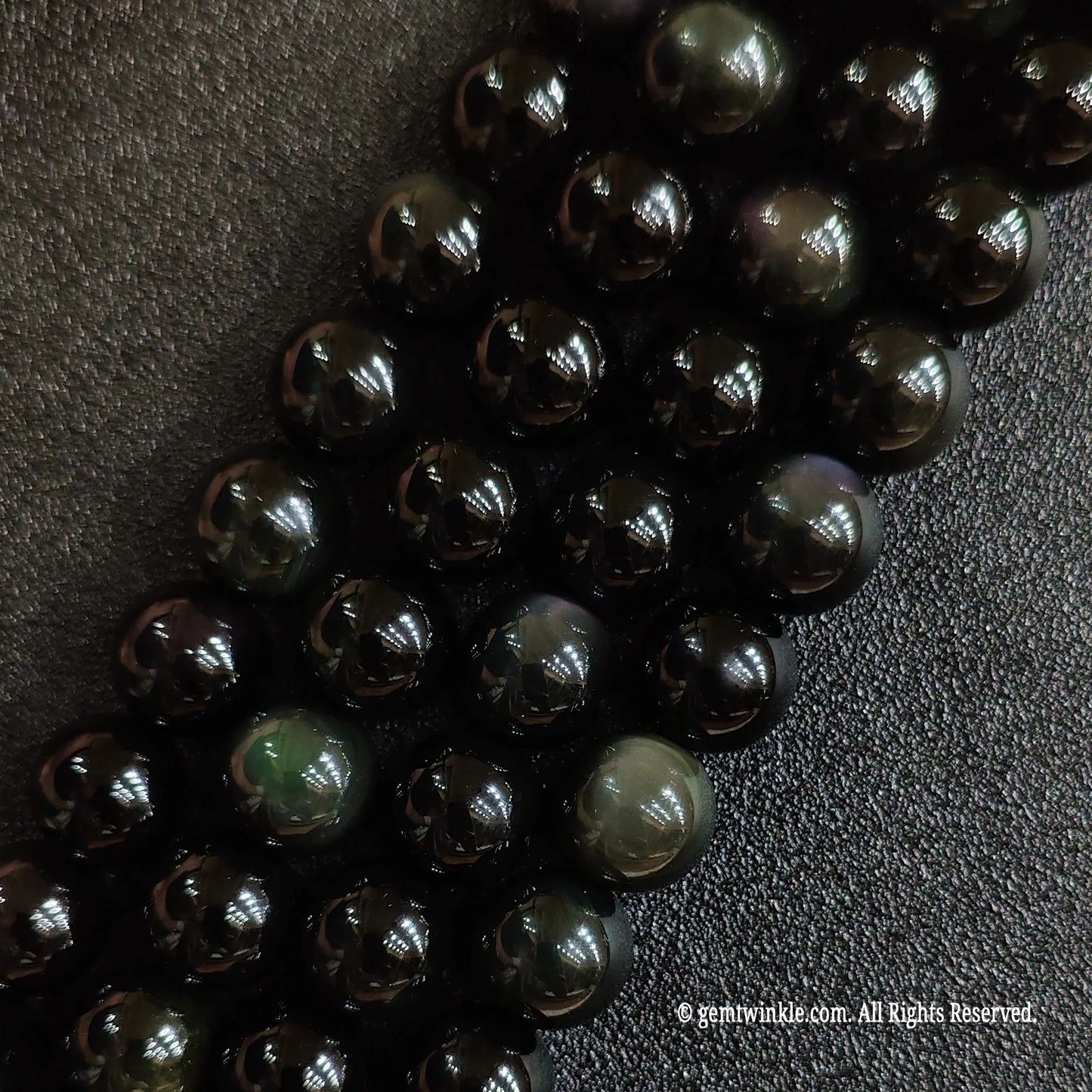 Close up view of natural rainbow obsidian crystal beads highlighting distinct circular green eye shimmer
