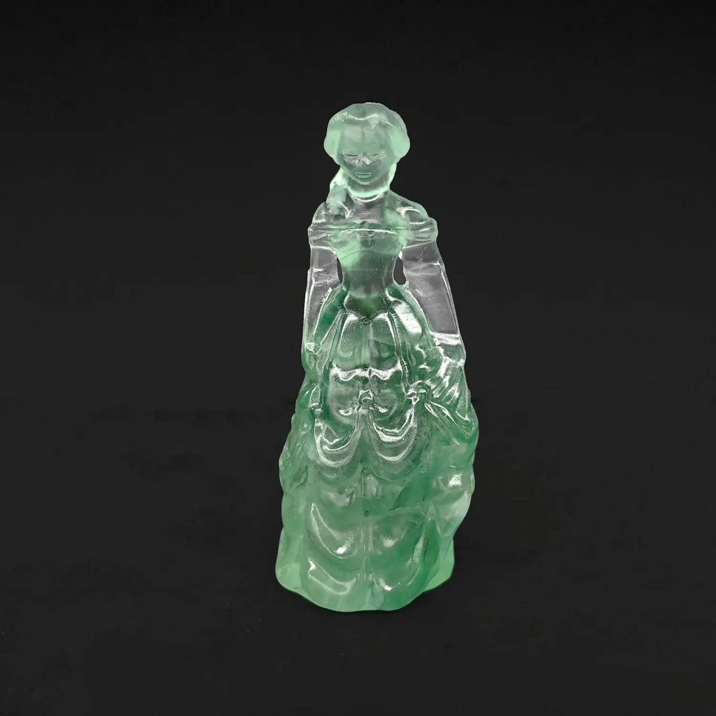 A 4-inch hand-carved natural green fluorite princess statue featuring a semi-translucent mint green tiered ball gown on a dark background