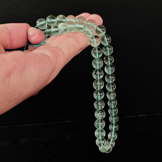 Hand holding natural green fluorite round loose beads strands for wholesale crystal jewelry making supplies.