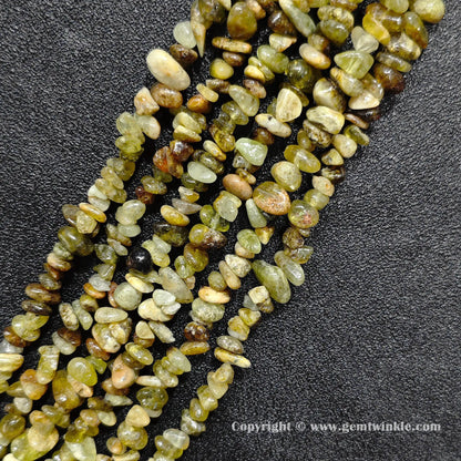 Angled view of tumbled green garnet freeform chip gemstone strands