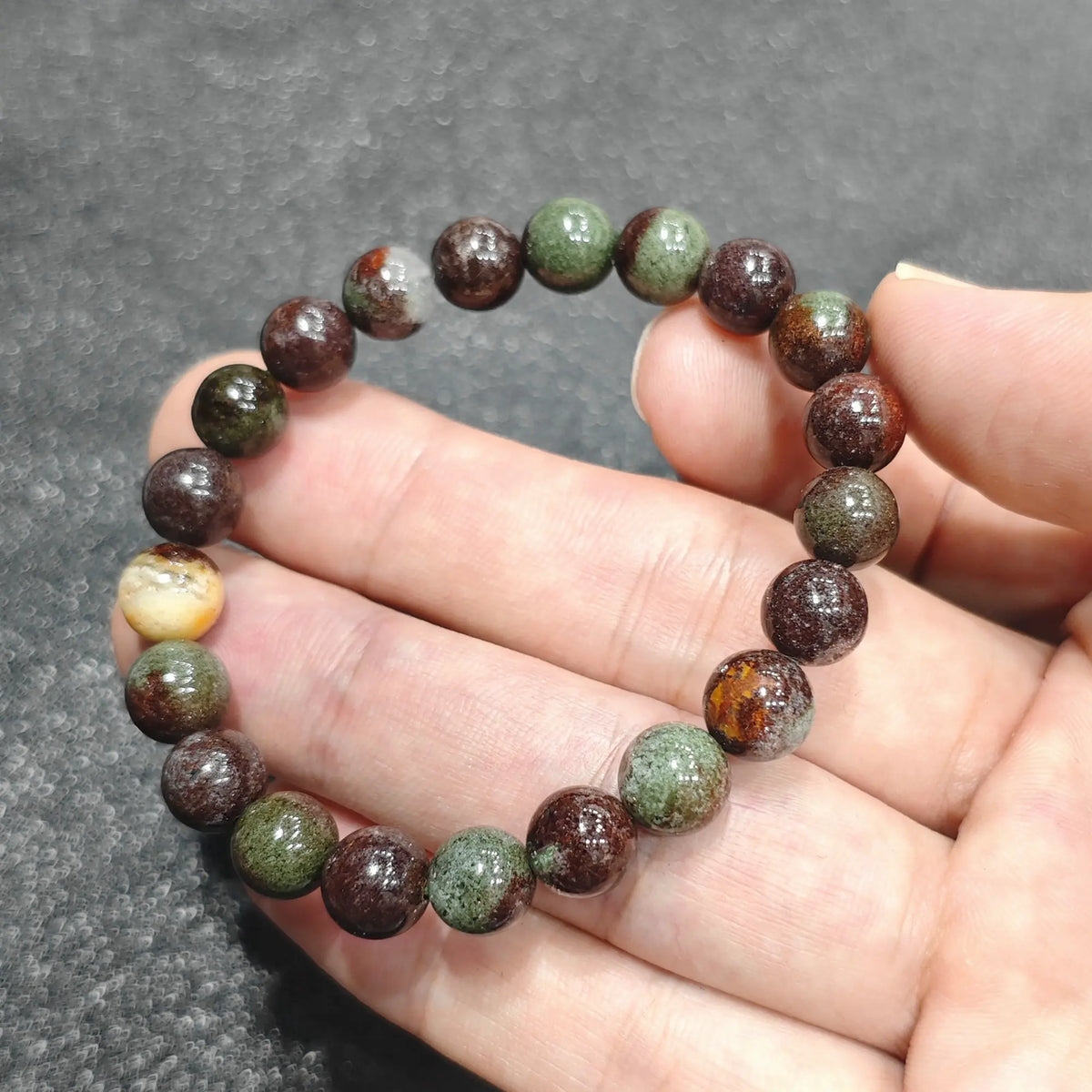 Close up view of a hand holding an 8mm natural green phantom quartz bracelet with red hematite matrix
