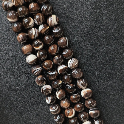 Natural grey mother of pearl round beads with brown banded swirl patterns macro view