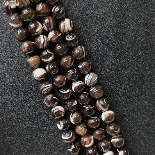 Natural grey mother of pearl round beads with brown banded swirl patterns macro view