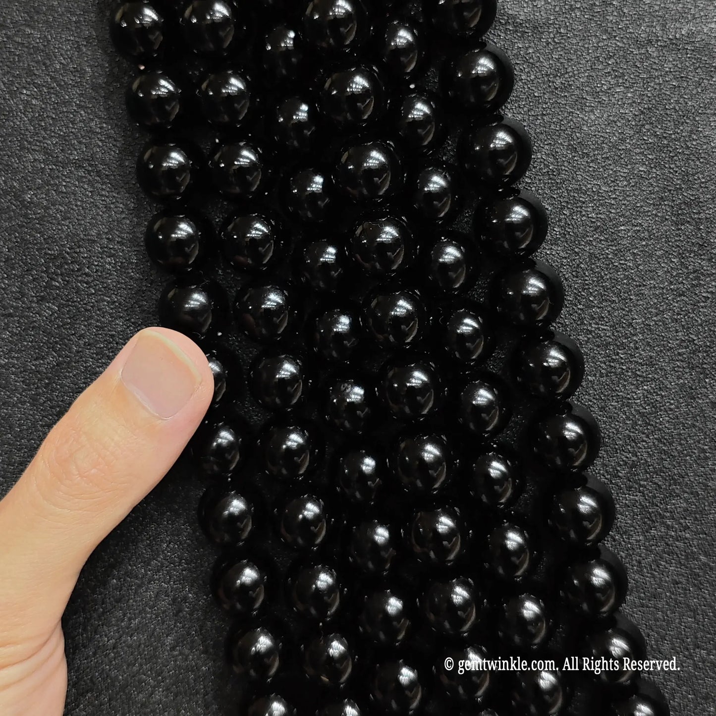 A finger pointing at multiple strands of natural pure black obsidian crystal beads to demonstrate texture and shine