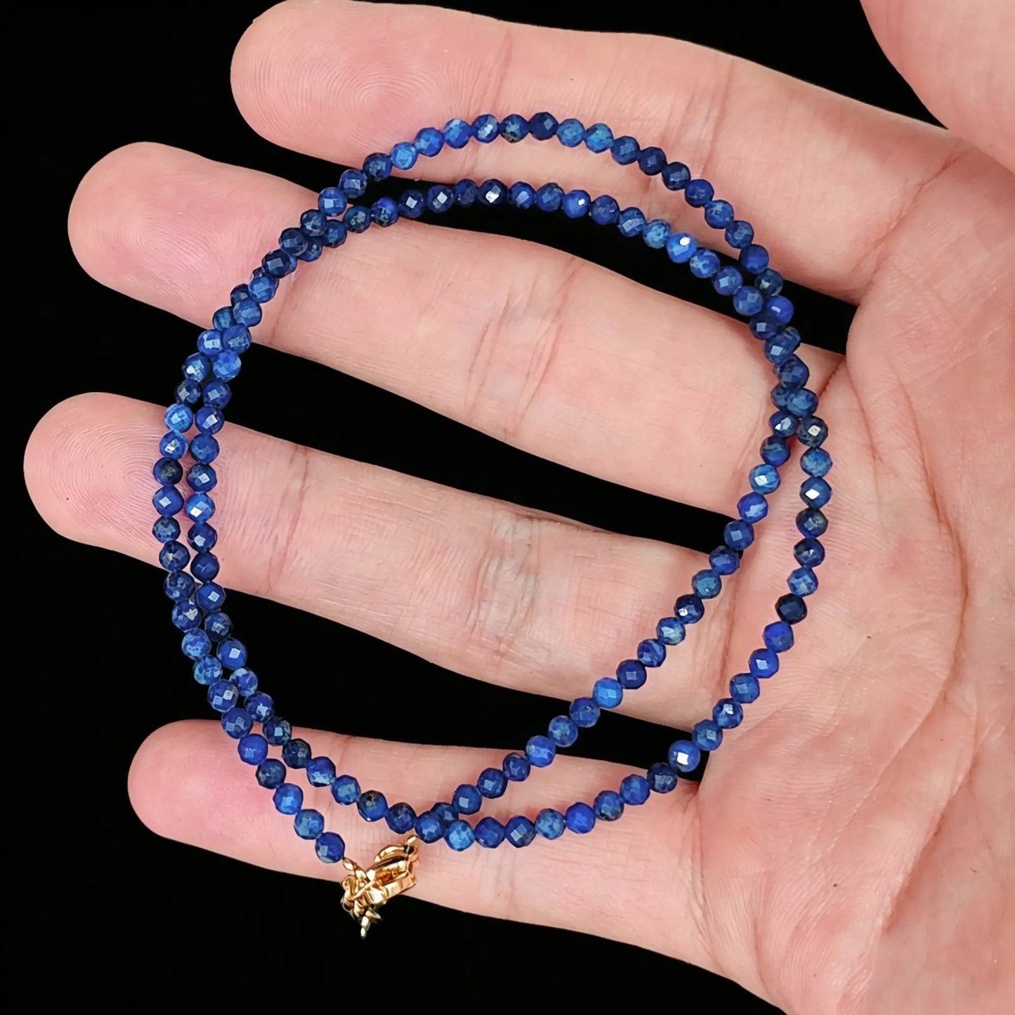 3-4mm natural lapis lazuli faceted bead strand held in hand displaying royal blue color
