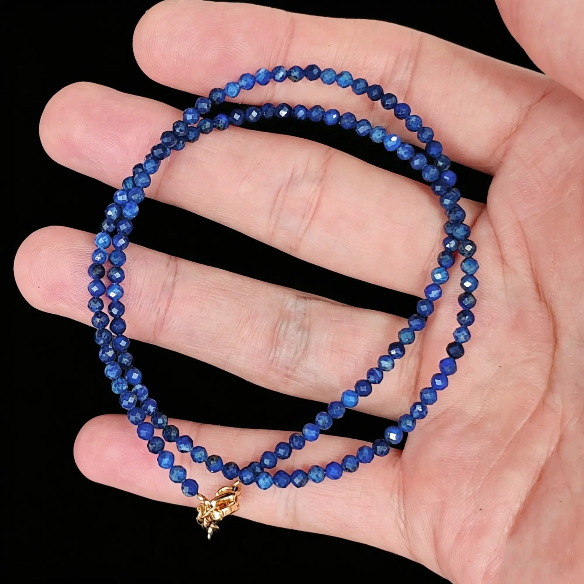 3-4mm natural lapis lazuli faceted bead strand held in hand displaying royal blue color
