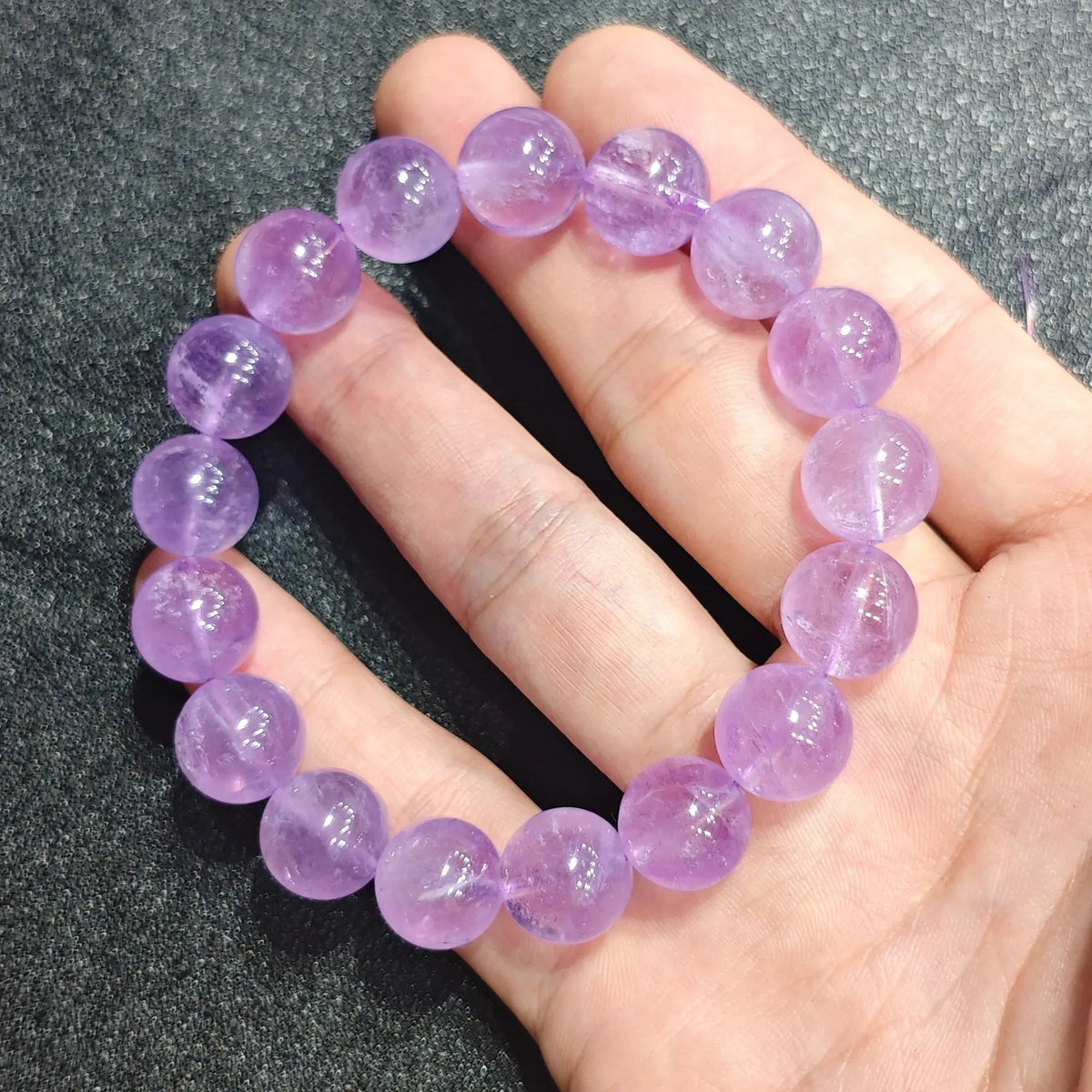 Close up view of a hand holding a natural lavender amethyst bracelet crafted with 12mm translucent soft lilac beads[cite: 9]