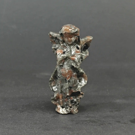 A hand-carved natural matrix granite praying guardian angel statue displaying a rustic mottled gray and brown stone texture on a dark background