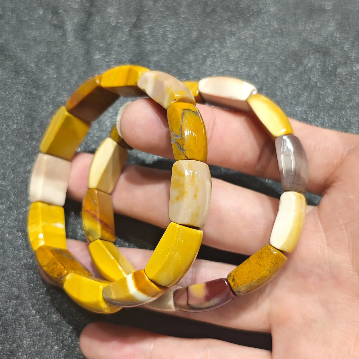 Hand holding a natural mookaite jasper bracelet crafted with 16mm egg yolk yellow and cream cylinder barrel beads