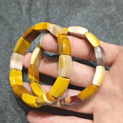 Hand holding a natural mookaite jasper bracelet crafted with 16mm egg yolk yellow and cream cylinder barrel beads