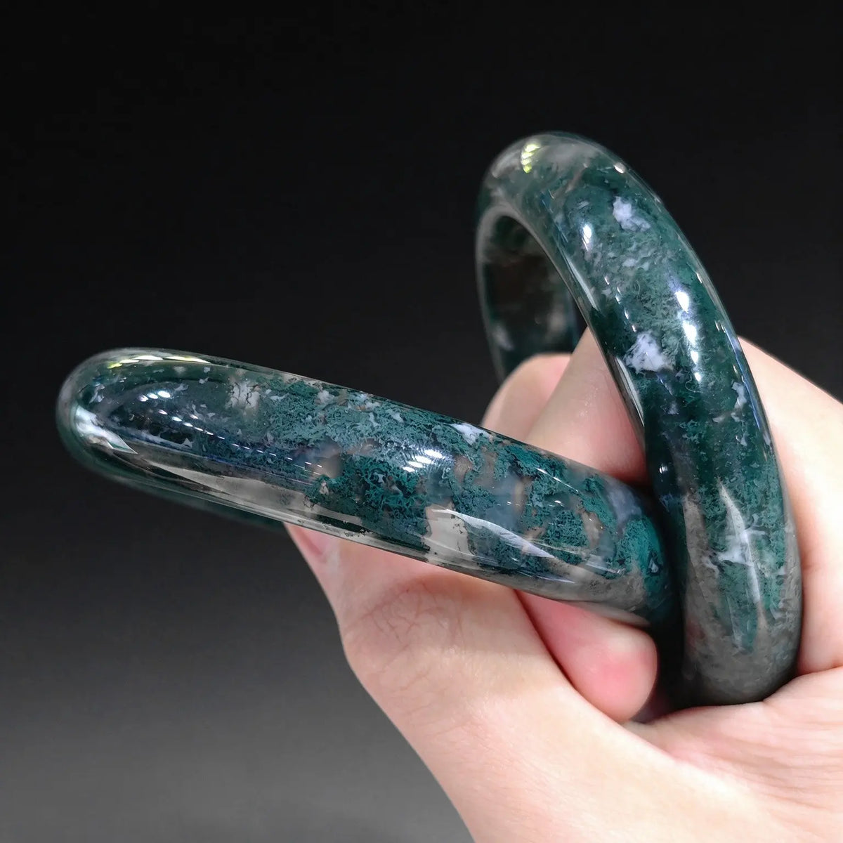Hand holding two natural moss agate solid bangles displaying rich dark green dendritic chlorite patterns