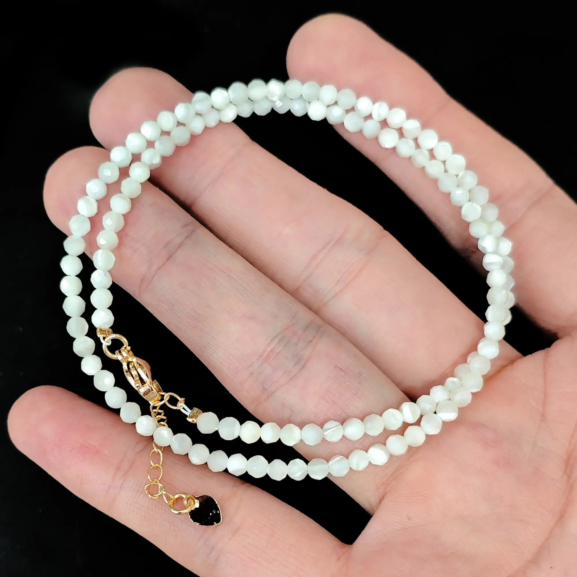 close up of gold lobster clasp and heart tag on white mother of pearl shell strand
