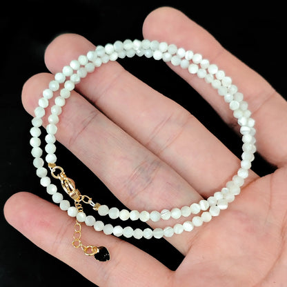 close up of gold lobster clasp and heart tag on white mother of pearl shell strand