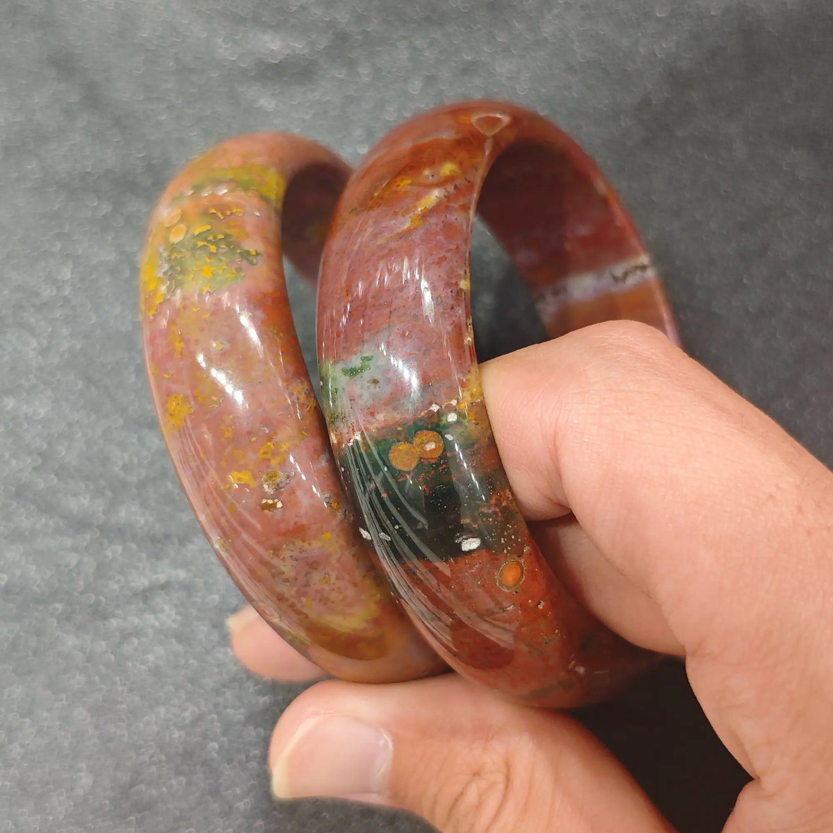 Natural Ocean Jasper solid gemstone bangle bracelet held on hand displaying organic multicolored orbs and earth tones