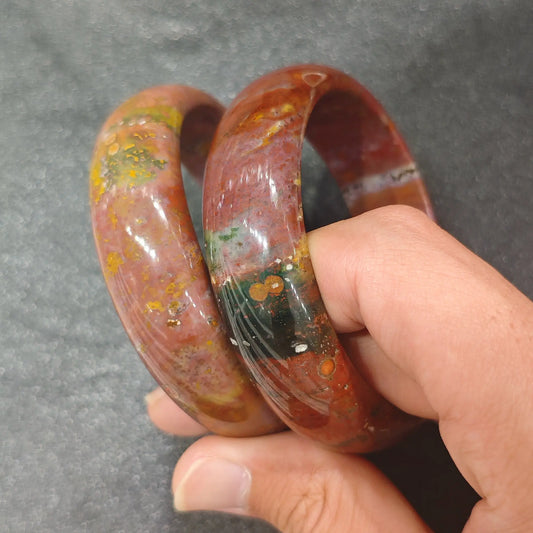 Natural Ocean Jasper solid gemstone bangle bracelet held on hand displaying organic multicolored orbs and earth tones