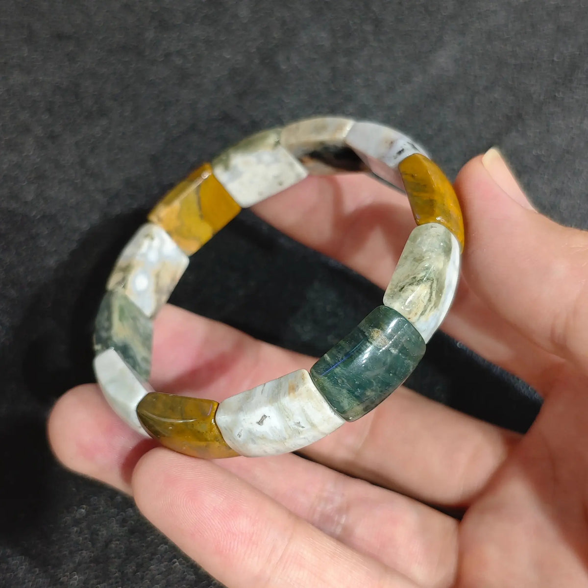 Natural ocean jasper rectangle plate bead stretch bracelet held on hand showing smooth green yellow and cream orbicular patterns