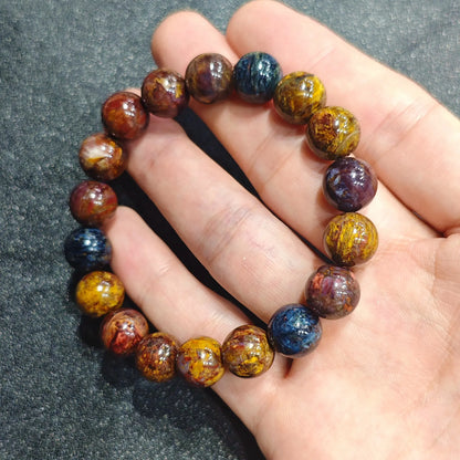 Close up view of a hand holding a natural pietersite bracelet crafted with 10mm mixed blue, gold, and brown spherical beads