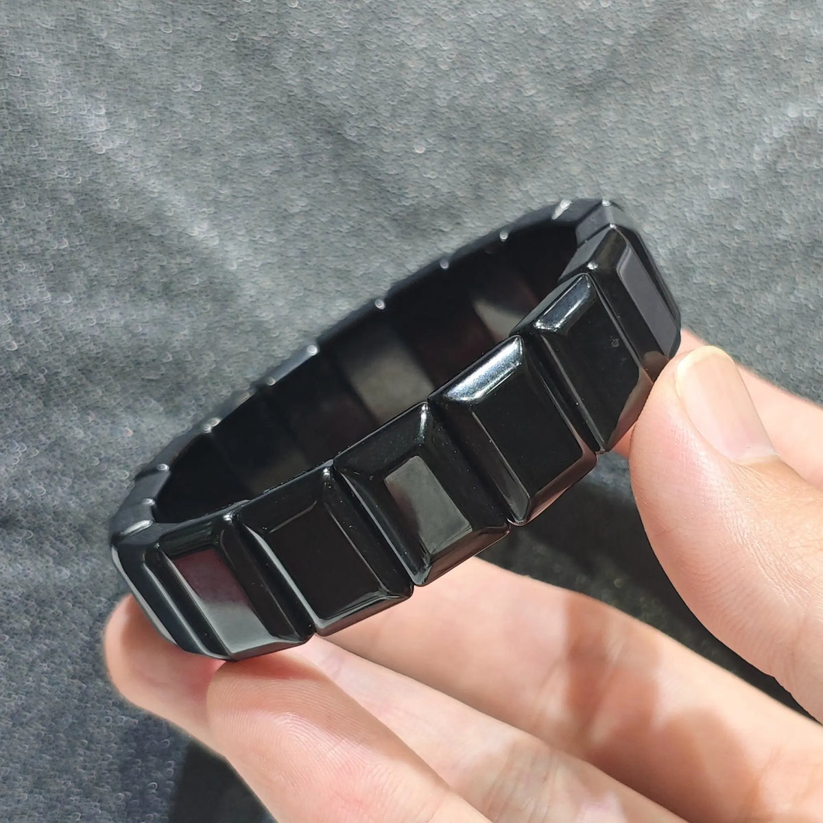 Hand holding a natural pure black obsidian plate bead bracelet with high gloss surface finish