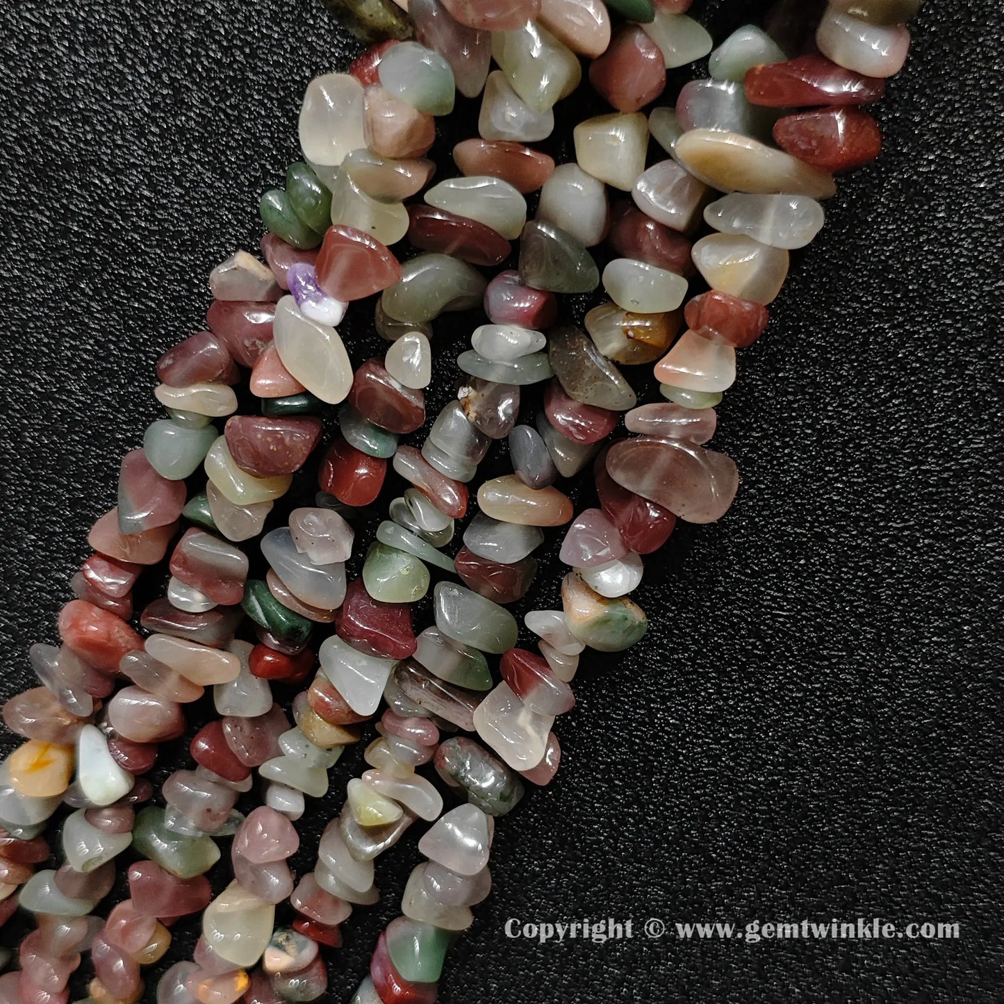 Angled view of tumbled purple and green agate freeform chip gemstone strands