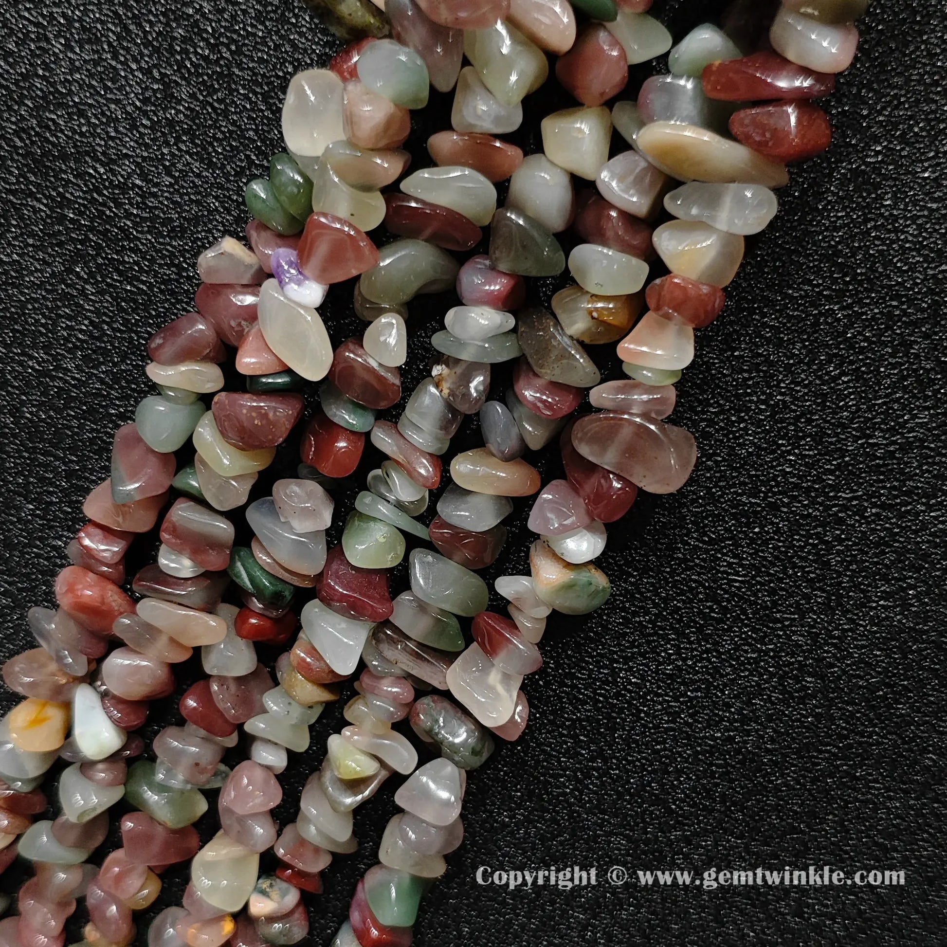 Angled view of tumbled purple and green agate freeform chip gemstone strands